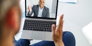 Man video chatting on laptop, waving hands.
