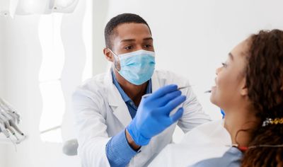Dentist examining a patient's mouth wearing protective mask and gloves.