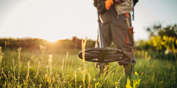 Person using a metal detector in a sunlit field.