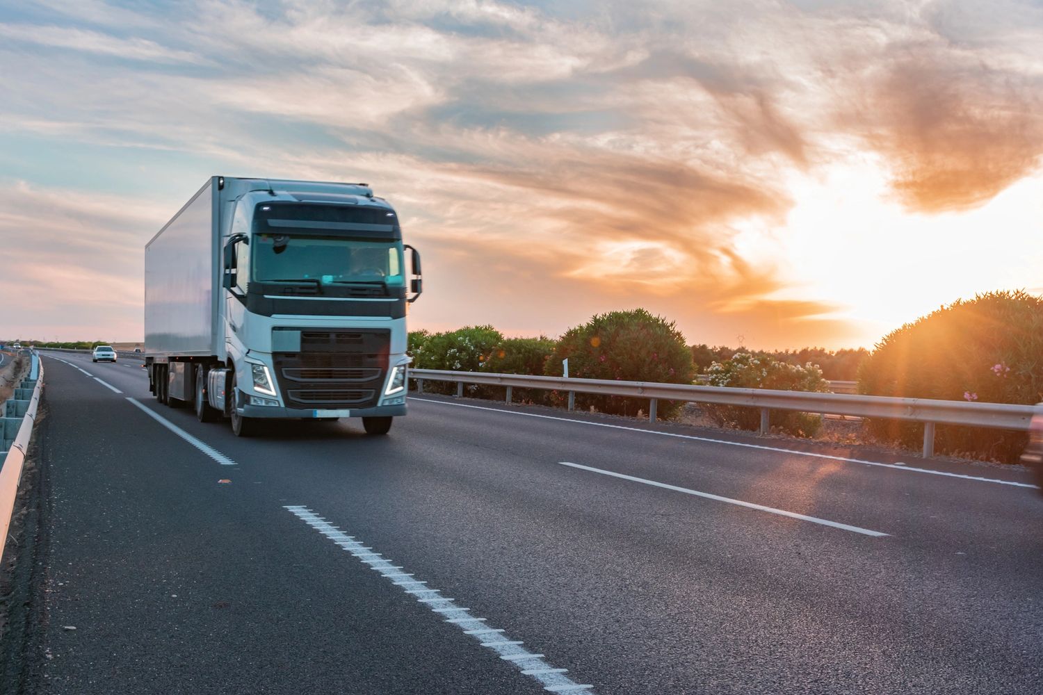 A white truck driving on a highway at sunset.