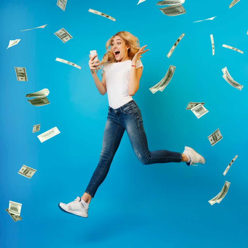 Online Lottery. Creatife Collage Of Overjoyed Woman Jumping With Smartphone Under Money Shower, Celebrating Victory, Full-Length Shot