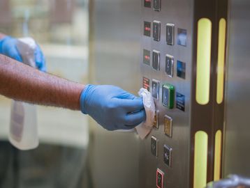 Person disinfecting elevator buttons with gloves.