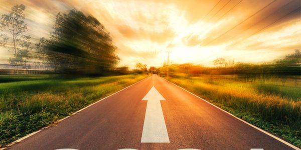 A road with a forward arrow under a bright, blurred sunset sky.