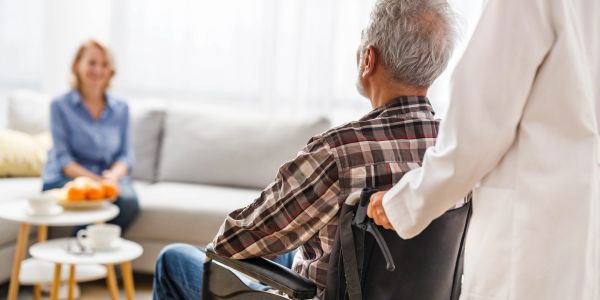 Caregiver assisting elderly man in wheelchair at home.