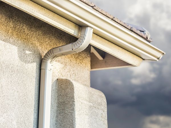 Close-up of a house gutter and downspout under cloudy skies.