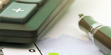 Close-up of a calculator, pen, and paper on a desk.