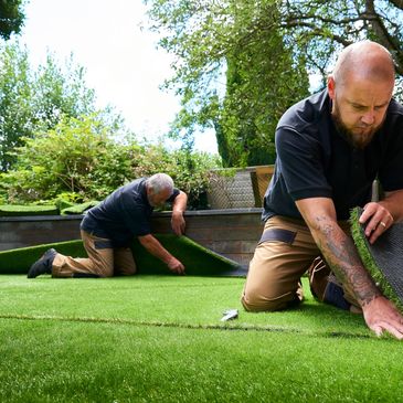 Two men installing artificial grass outdoors.