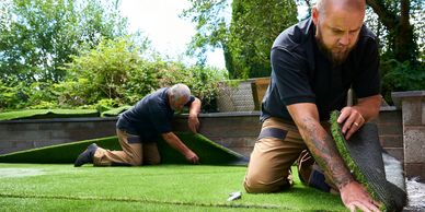 Two men installing artificial grass outdoors.