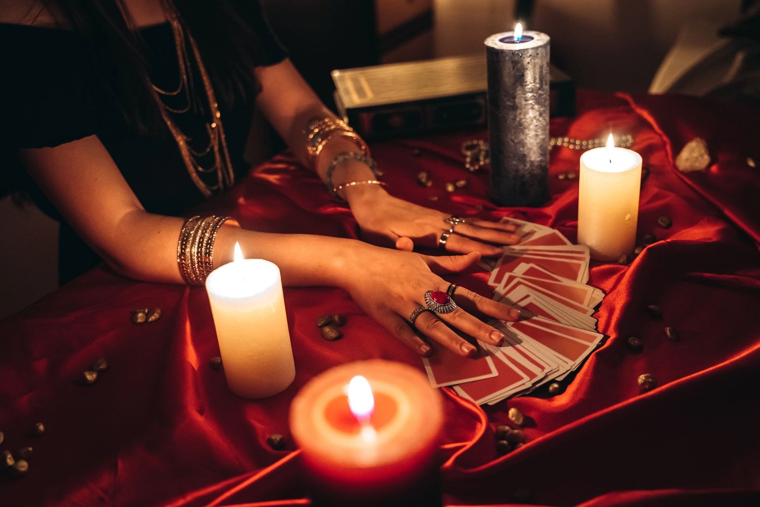 Person reading tarot cards by candlelight on a red cloth.