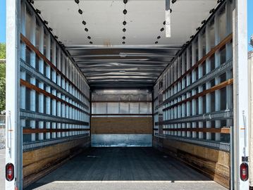 Empty box truck with open rear doors under clear blue sky.