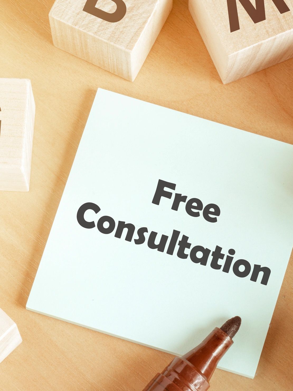 Sticky note with 'Free Consultation' written, surrounded by wooden blocks and a marker.