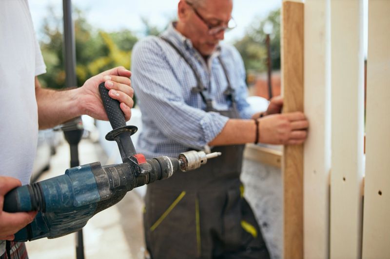 Two skilled construction manual workers installing a wooden fence.