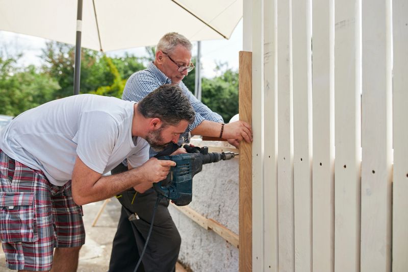 Two skilled construction manual workers installing a wooden fence.
