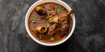 A bowl of rich mutton curry garnished with coriander leaves.