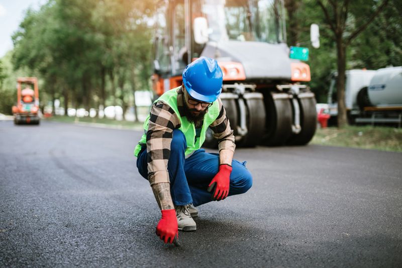 Young bearded male road construction worker on his job. Bright sunny day. Strong light.