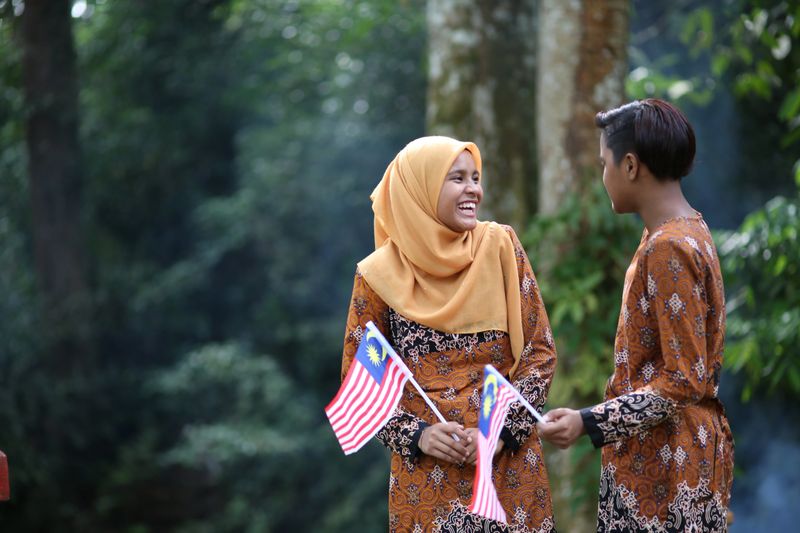Muslim Indian ethnicity teenage girls are enjoying nature reserve environment while holding Malaysia flag cheerfully.