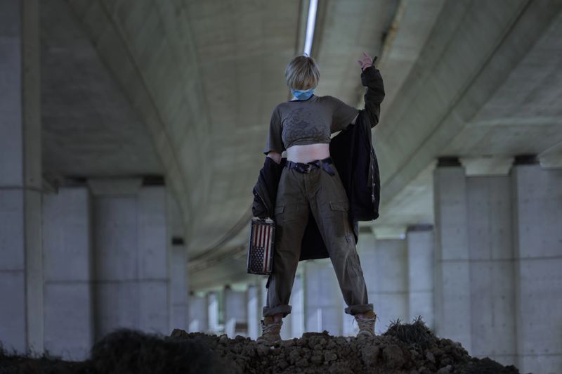 Woman in a military-like outfit in mask holding a case with the american flag on it