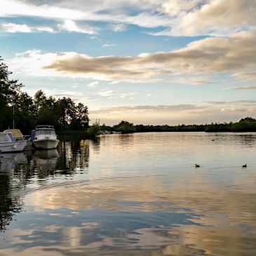 Boats docked on a calm river with a partly cloudy sky.