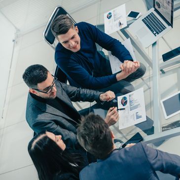 Four professionals discussing charts and graphs around a glass table in an office.