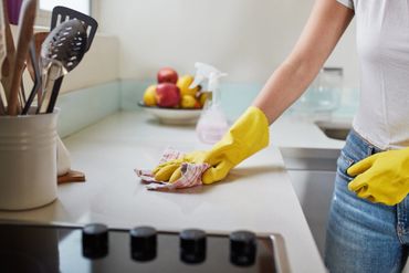 Person cleaning a kitchen counter wearing yellow gloves.