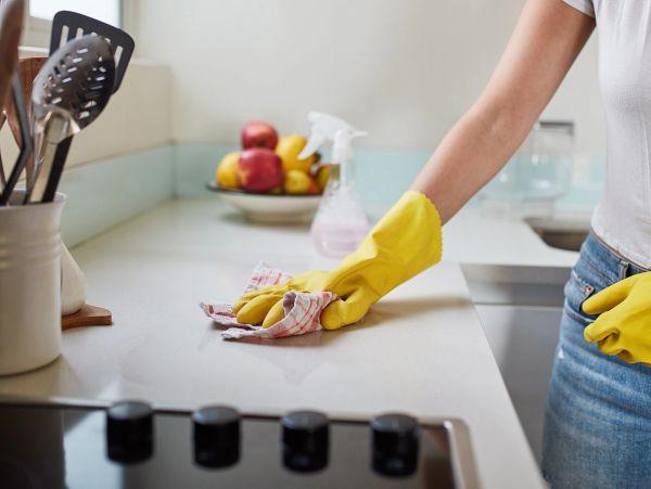 Person cleaning kitchen countertop with yellow gloves.