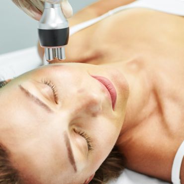 Woman receiving a facial treatment with a handheld device.