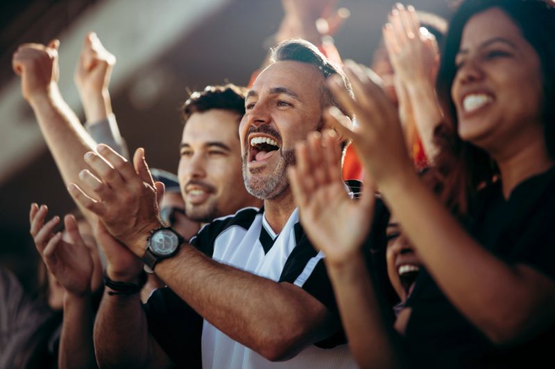 Group of men and women cheering their national team. Football team supporters enjoying during watching a live match from stadium.