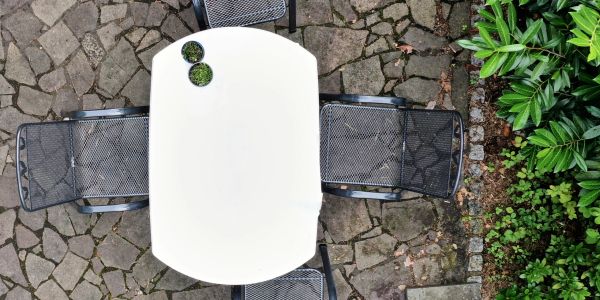White outdoor table with four metal chairs on stone patio.