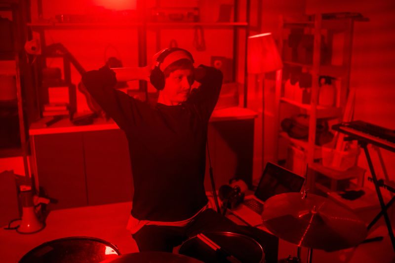 Young restful musician in casualwear and headphones listening to the music he recorded in his studio while sitting by drumset