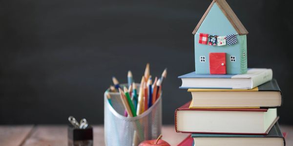 Stack of books with a small house model on top and colored pencils.