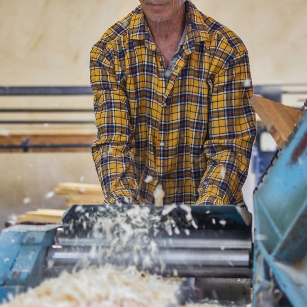 Man wearing safety goggles operates woodworking machine in workshop.