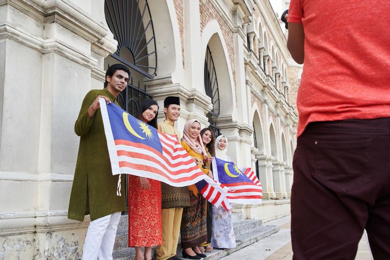 photographer taking photograph of Malaysia multi ethnic adults holding malaysia flag celebrating their independence day at merdeka square