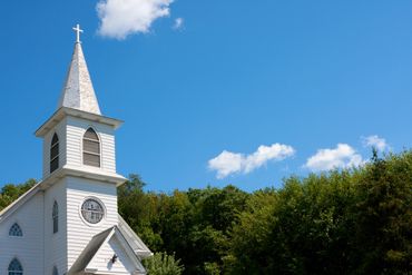 White church steeple with a cross against a blue sky.