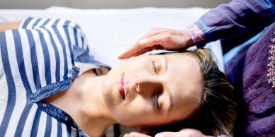 Person lying down with eyes closed and hands near their head.