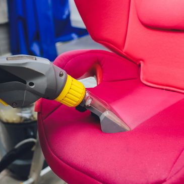 Cleaning a red fabric car seat with a vacuum tool.