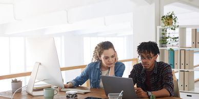 Two young professionals collaborating on a laptop in a bright office.