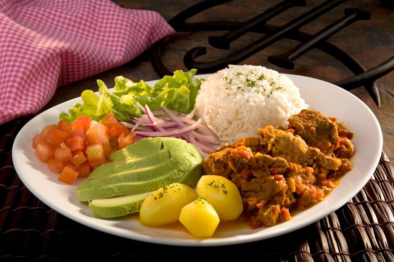 Dry goat, traditional Ecuadorian dish  called "Seco de Chivo", accompanied by potatoes, avocado, diced tomato, onions, lettuce and rice. Food still life.