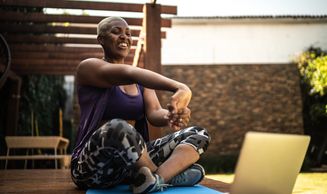 Woman stretching and exercising outdoors while watching a laptop.