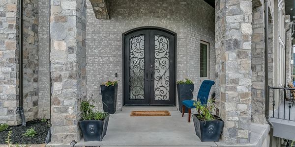 Elegant stone porch with intricate black double doors.