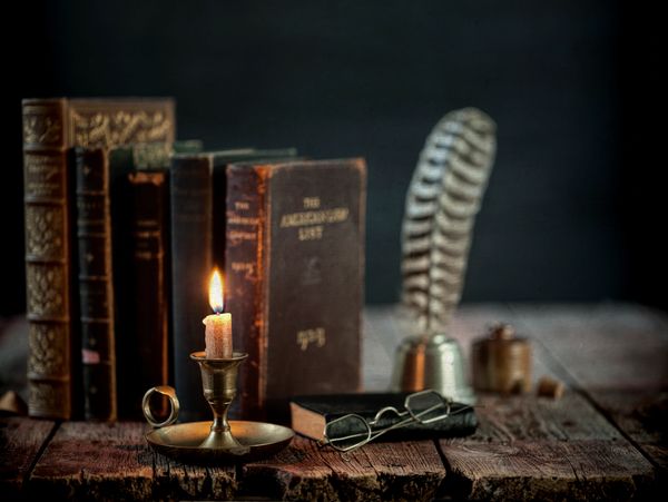 Vintage books, a burning candle, and old spectacles on a rustic wooden table.