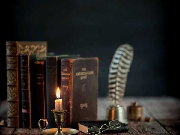 Vintage books, a lit candle, and reading glasses on a rustic wooden table.