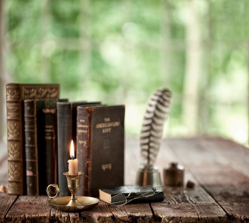 Vintage study area with books, quill pen and candle on an old wood desk in front of a window