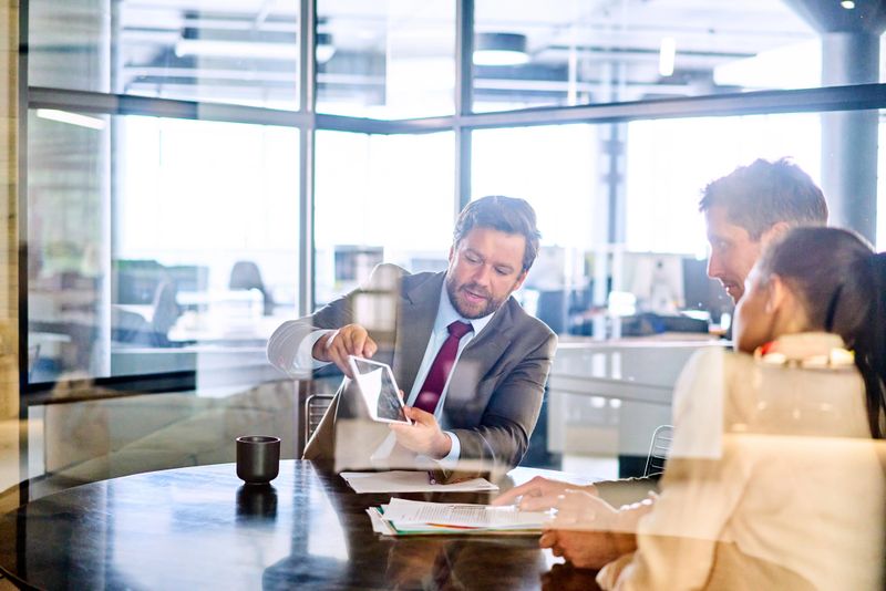 Financial advisor showing something on a digital tablet to a young couple during a meeting inside of his office