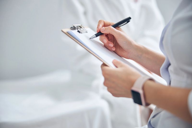 Close up portrait of female doctor hands holding clipboard while she writing notes with black pen