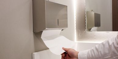 Hand pulling paper towel from dispenser in a bathroom.