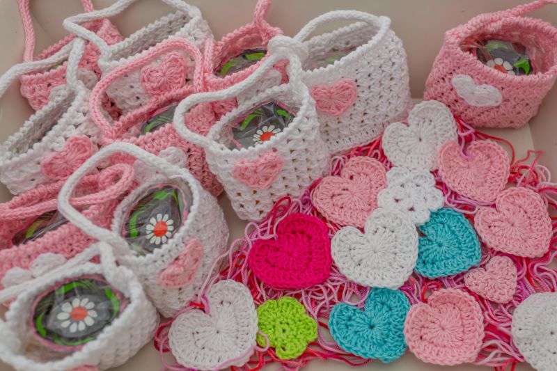 Small pink and white crochet souvenirs for christening or first communion, mini bags, mini hearts and mini flowers in different colors on some threads, handmade craft creativity