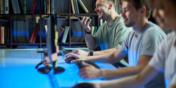 Three young men working at computers in a modern, tech-focused environment.