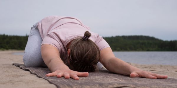Person practicing yoga stretch on a beach mat near water.