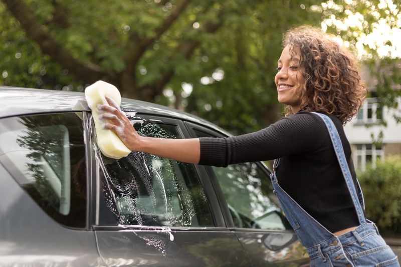 Young woman washing car on driveway
