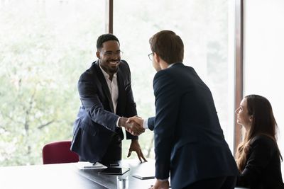 Man shaking hand of another man at a desk with a woman looking